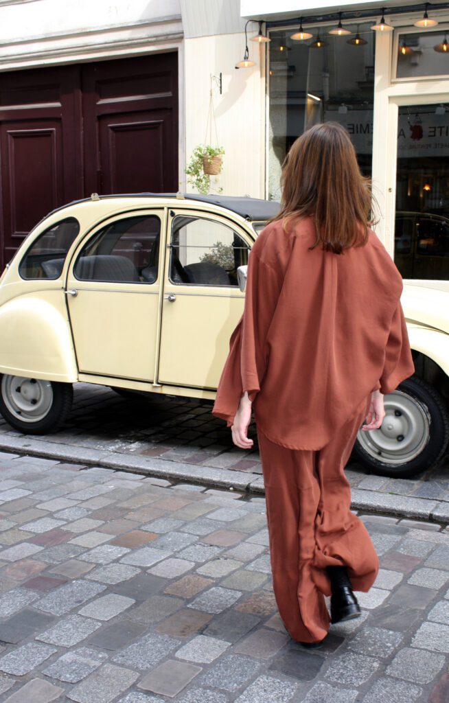 The back of a woman walking through a street in Paris. She is wearing a matching set consisting of a blouse and wide pants in Maroon.
